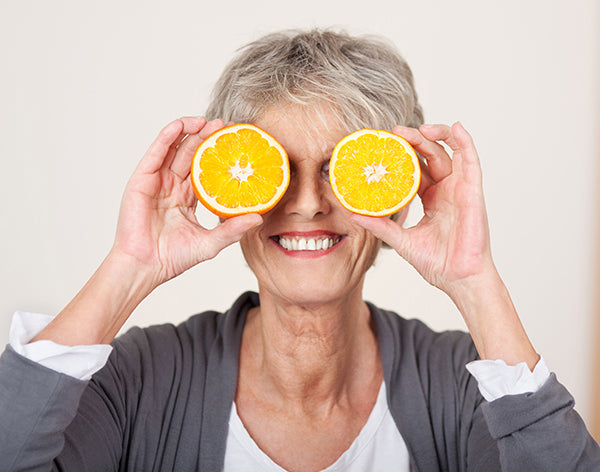 Senior Woman Holding Half Oranges Over Eyes
